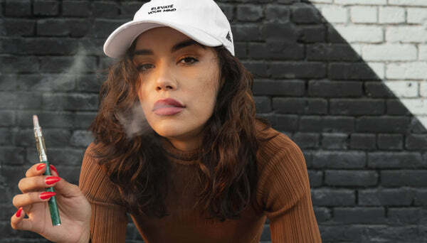 Woman wearing a hat and vaping a Delta-8 cartridg